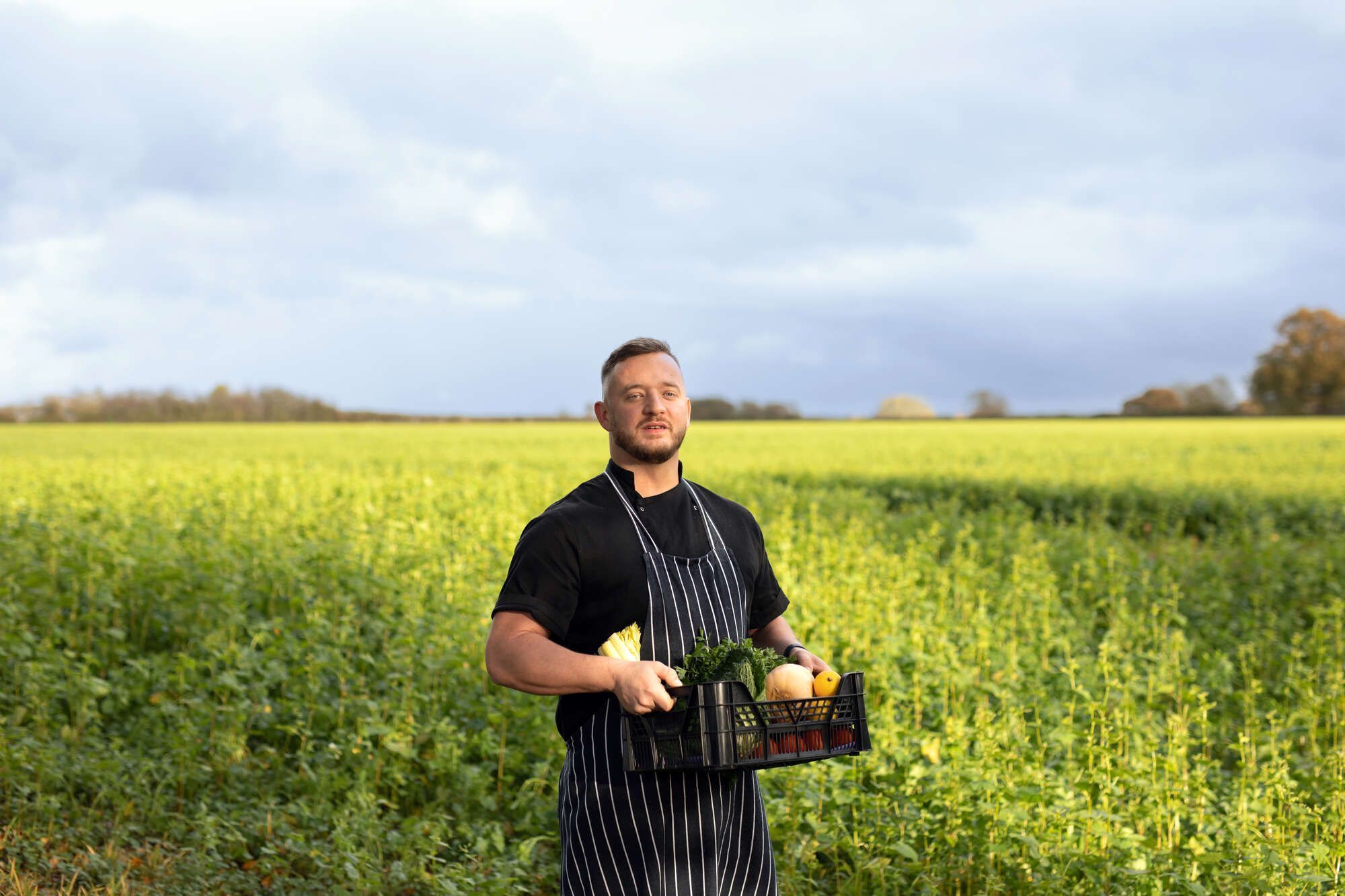 man holding a tray of assorted vegetables in a farmer's field