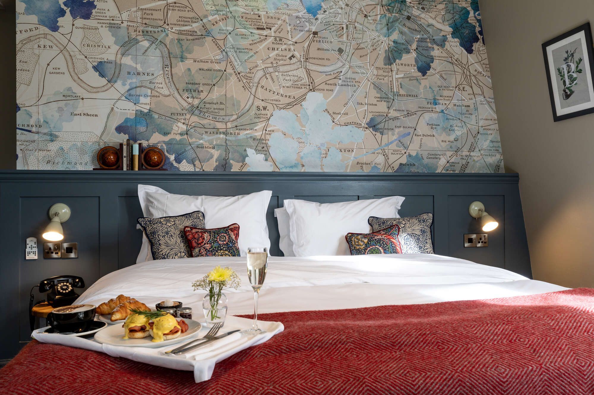 bedroom with map of England wallpaper and tray of eggs benedict, croissants, and champagne on the bed