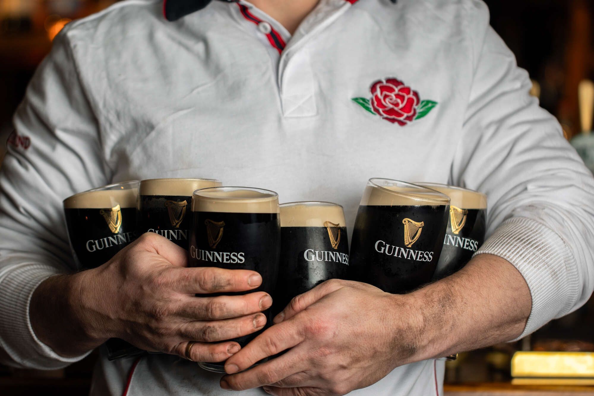 man in a white jumper cradling six pints of Guinness