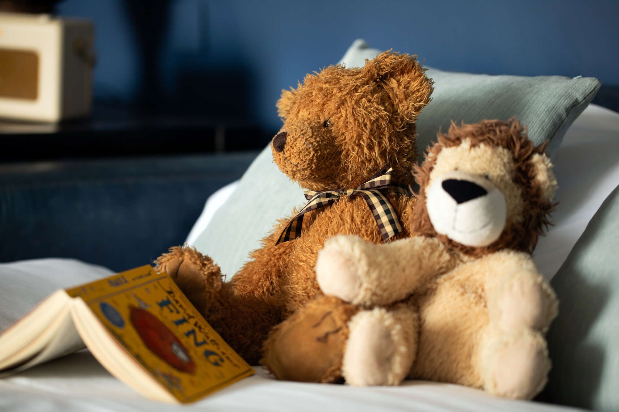 a stuffed bear and a stuffed lion sitting on a bed with an open book