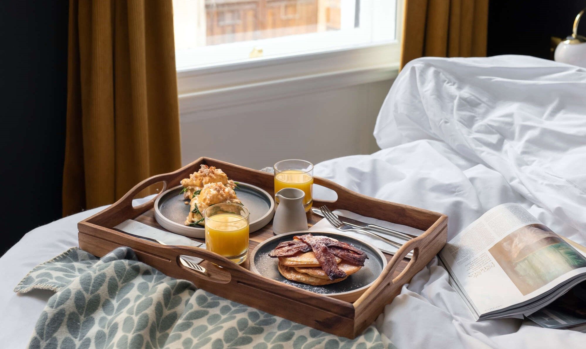 breakfast in bed with tray of pancakes, bacon, eggs benedict, and orange juice