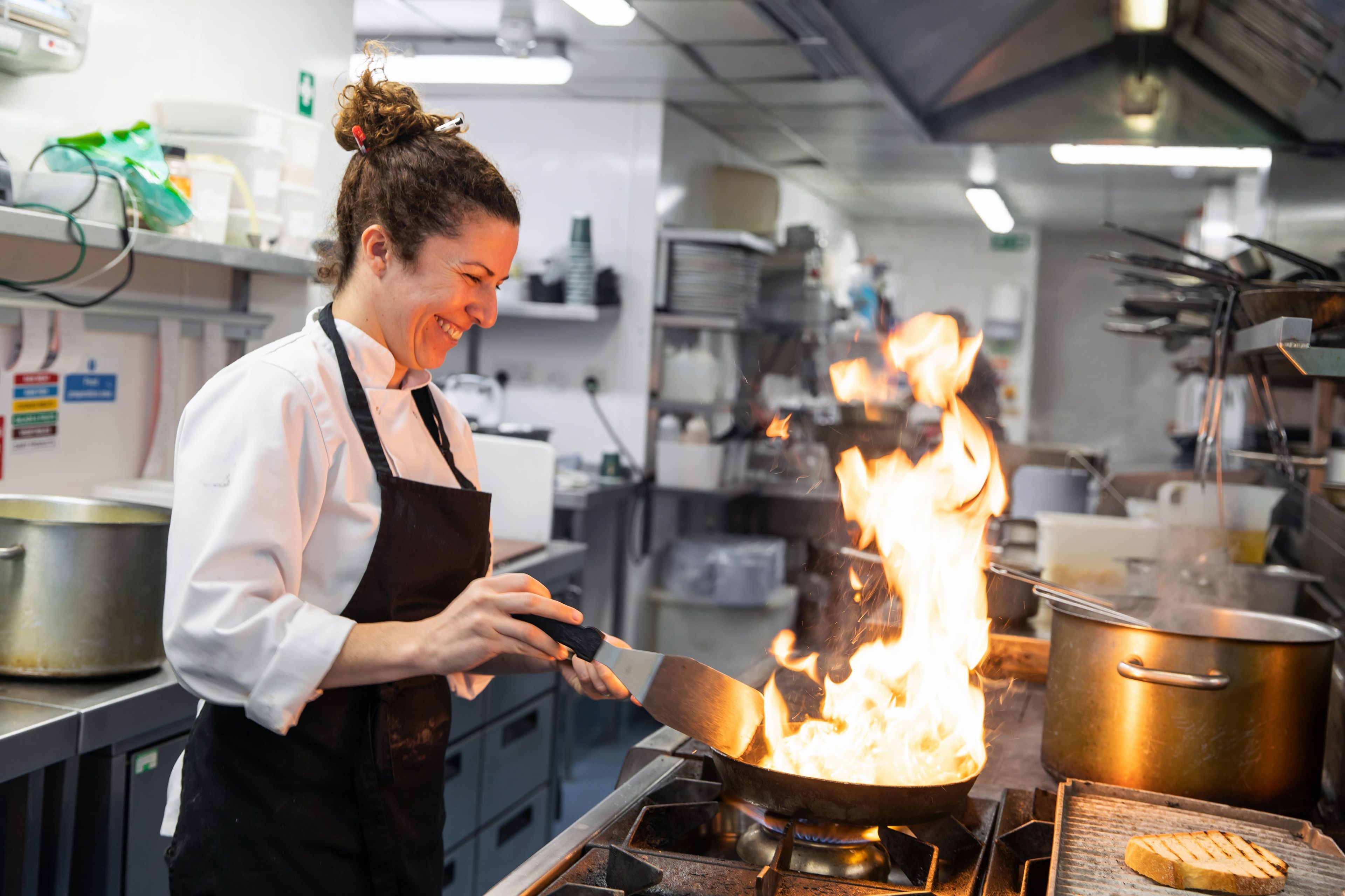 woman cooking food in a pan with a flame in a Young's kitchen