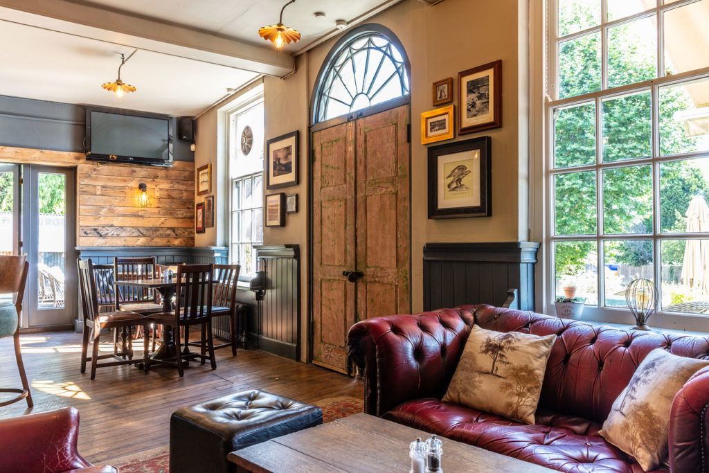 pub interior with tables, chairs, a red leather coach, and a view of the garden