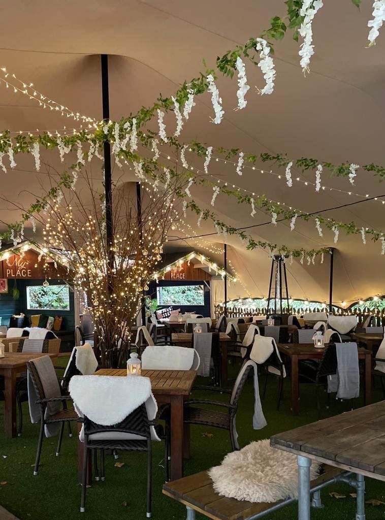 party tent with tables, chairs, lights, and floral garlands